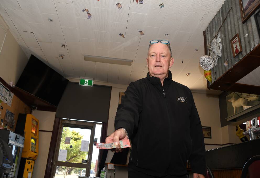 STICK: National Hotel publican Bill Lovell prepares to toss a $20 note into the ceiling of the building. Picture: ALEX DALZIEL